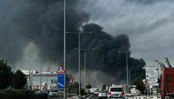 Motorists drive past a plume of smoke rising from a reported Iranian strike in the industrial dis...